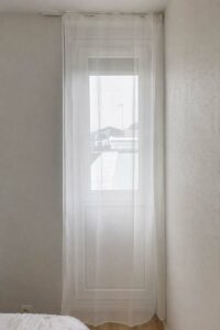 Voilage anti-ondes blanc posé devant une porte-fenêtre dans une chambre